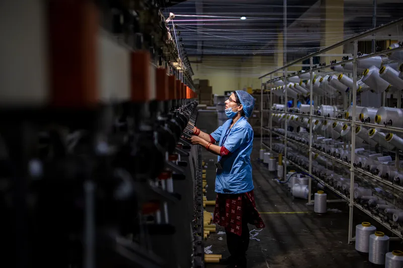 Textile worker operating rows of textile manufacturing machinery